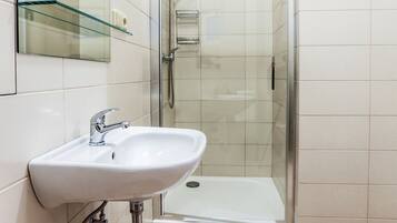 A modern bathroom with a glass shower enclosure, a white sink, and a glass shelf above the mirror.