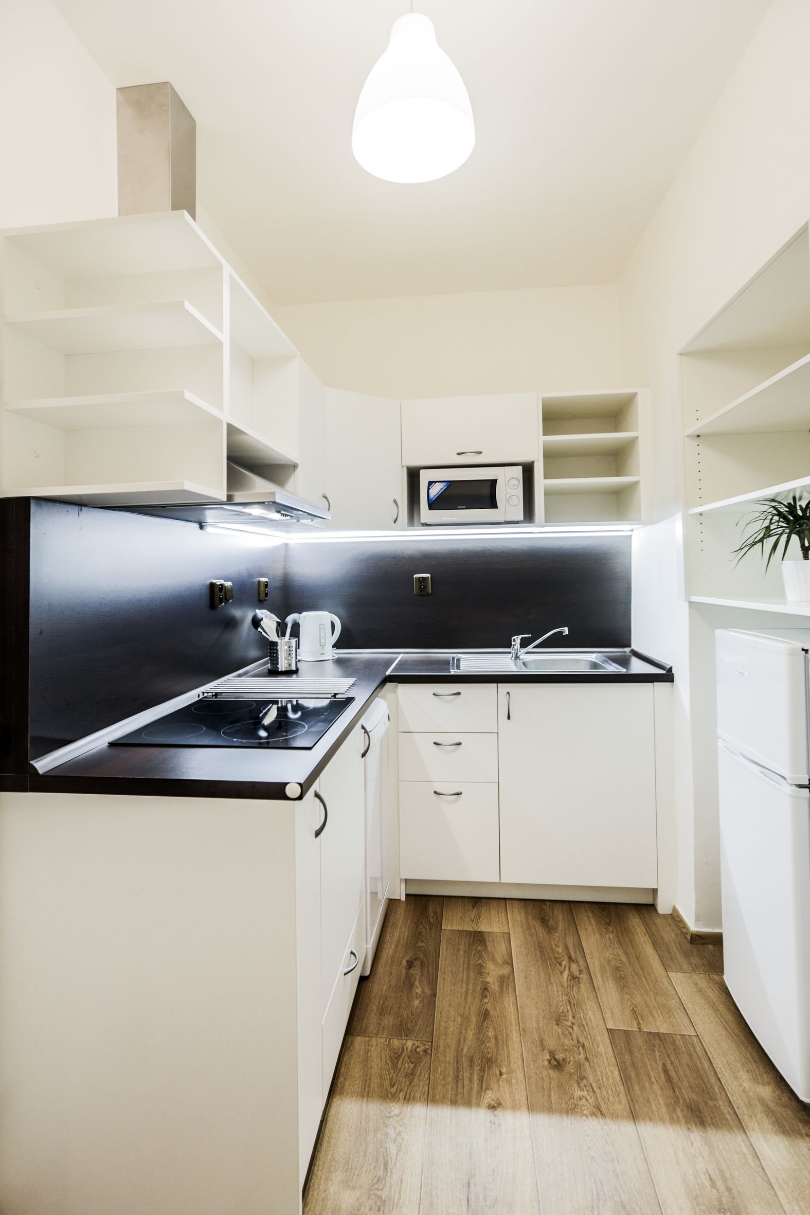A modern kitchen with white cabinetry, a black countertop, and a microwave.