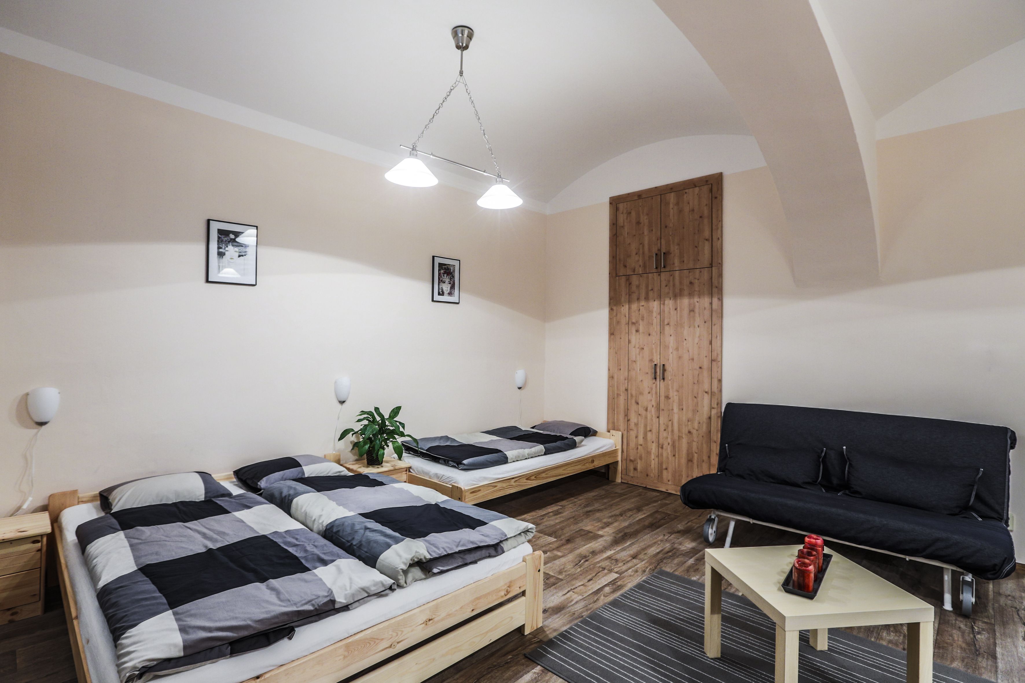 Una habitación con dos camas de madera, un sofá negro, una mesita con velas rojas y un armario de madera.