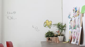 A room with a white wall decorated with drawings and text, a small potted plant, and a wooden display stand with photos.