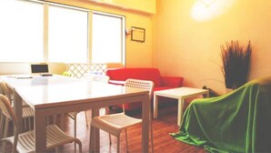 A room with a white table, chairs, a red sofa, and a small white table. - Kobe Sannomiya R2 Hostel (Kobe)