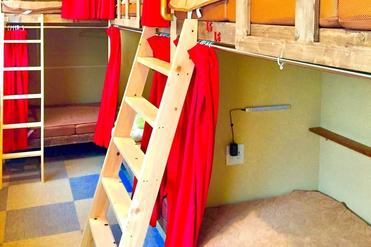 A dormitory room with bunk beds, a wooden ladder, and a red curtain.
