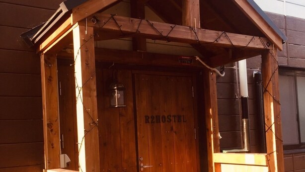 A wooden structure with a sloped roof, a door labeled "R2HOSTEL", and a small porch area. - Kobe Sannomiya R2 Hostel (Kobe)