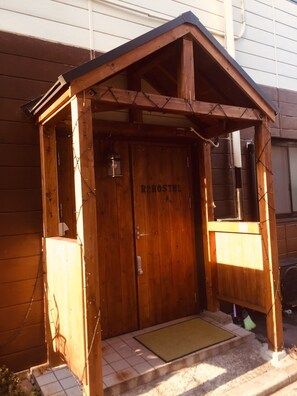A wooden structure with a sloped roof, a door labeled "R2HOSTEL", and a small porch area. - Kobe Sannomiya R2 Hostel (Kobe)