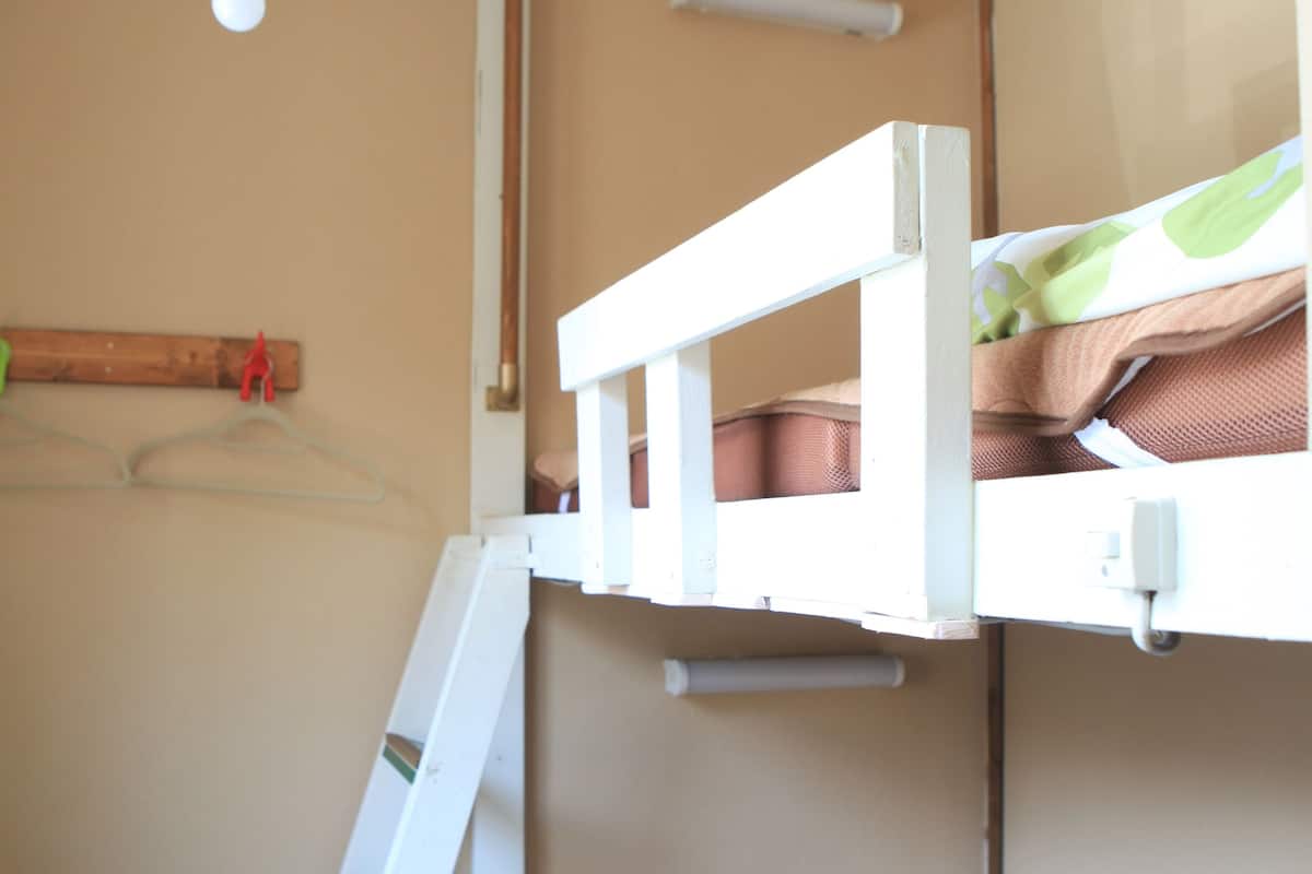 A bunk bed room with a ladder, a hanging light fixture, and a wooden hanger.