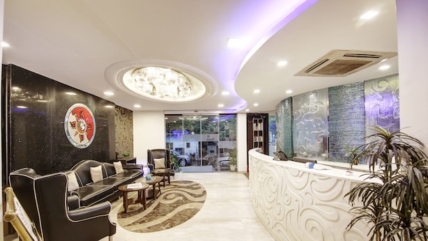A modern reception area with a black leather sofa, a round coffee table, and a white reception desk. - Hotel Good Times (New Delhi)
