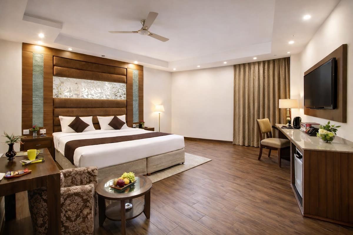 A hotel room with a bed, desk, chair, TV, and a ceiling fan.