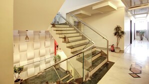 A modern interior with a glass staircase, potted plants, and a clean, minimalist design. - Hotel Good Times (New Delhi)