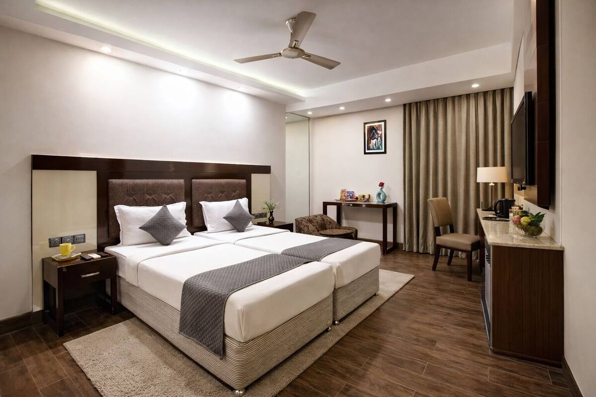 A hotel room with a large bed, bedside tables, a desk with a chair, a ceiling fan, and a TV.