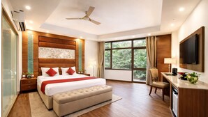 A modern hotel room with a large bed, a desk, a chair, a television, and a large window. - Hotel Good Times (New Delhi)