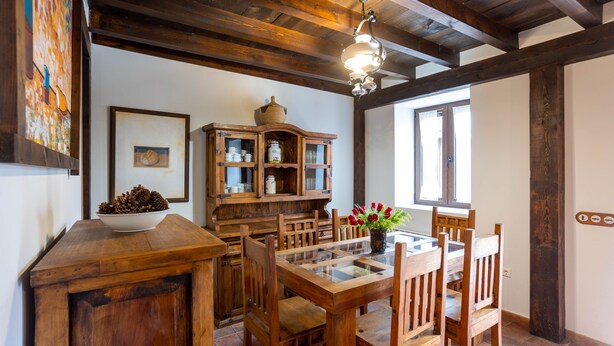 A wooden dining area with a glass-top table, wooden chairs, a cabinet with glass doors, and a chandelier. - Casa Rural Casa Adolfo (Santa Inés)