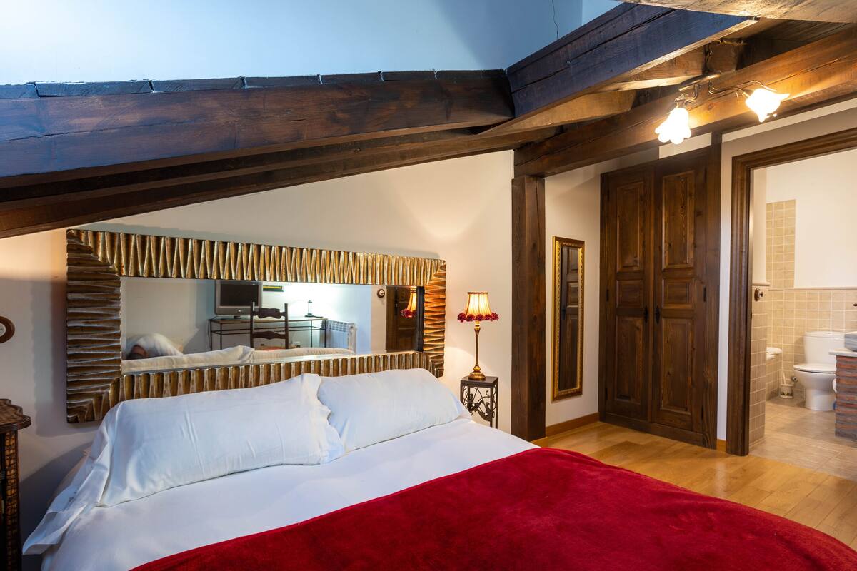 A bedroom with a bed, a mirror, a lamp, and a wooden ceiling.