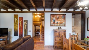 A living room with a brown leather sofa, wooden dining table with chairs, a television, and artwork on the walls. - Casa Rural Casa Adolfo (Santa Inés)