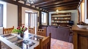 A cozy living room with a wooden ceiling, a glass dining table, a leather sofa, and a bookshelf filled with books. - Casa Rural Casa Adolfo (Santa Inés)