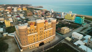 Una vista aerea di una cittadina costiera con un imponente edificio simile a un castello, caratterizzato da numerose torri e un cortile centrale.