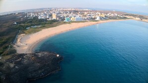 Vista aerea di una città costiera con spiaggia, edifici e un promontorio roccioso.