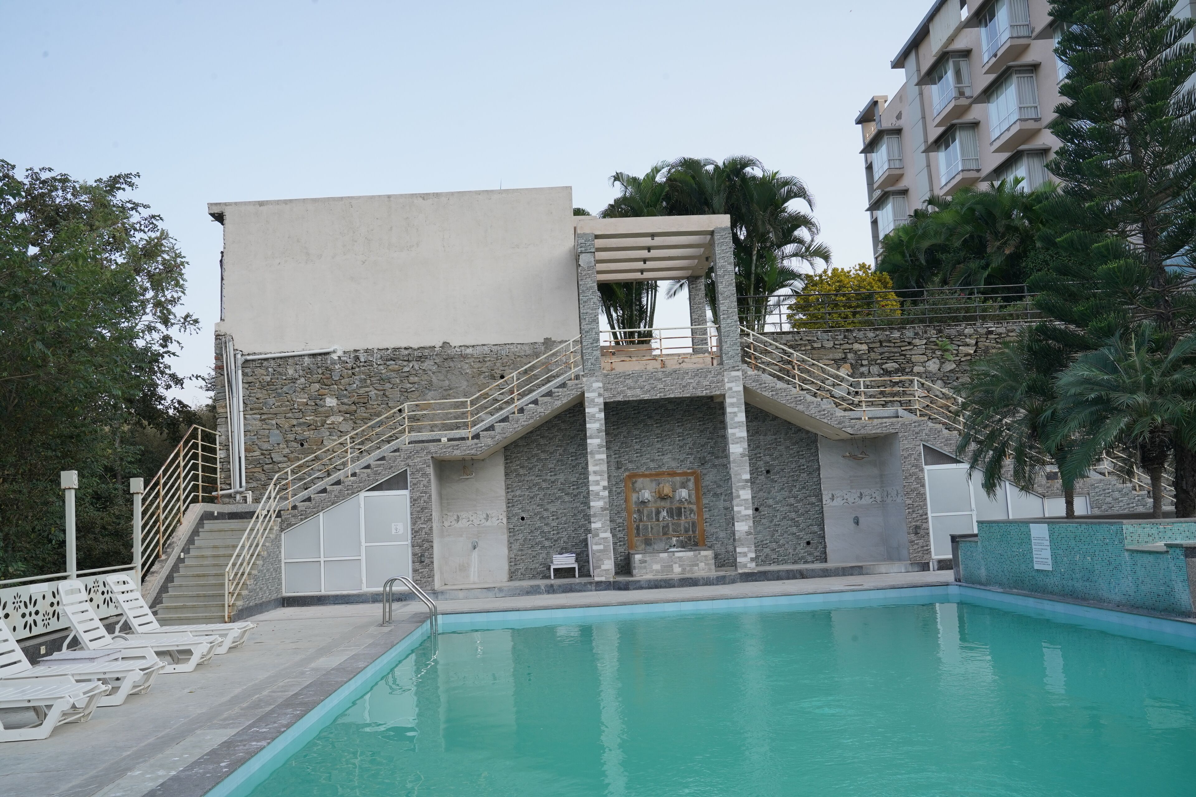 Ein Pool mit einer Steinmauer und einer Treppe, die zu einem überdachten Bereich führt.