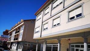 A hotel with a covered entrance, multiple floors, and a sign indicating it is a hotel and arena. - Hotel Arenal (Fisterra)
