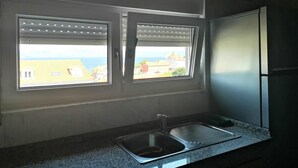 A kitchen with two windows, a stainless steel sink, and a refrigerator. - Hotel Arenal (Fisterra)