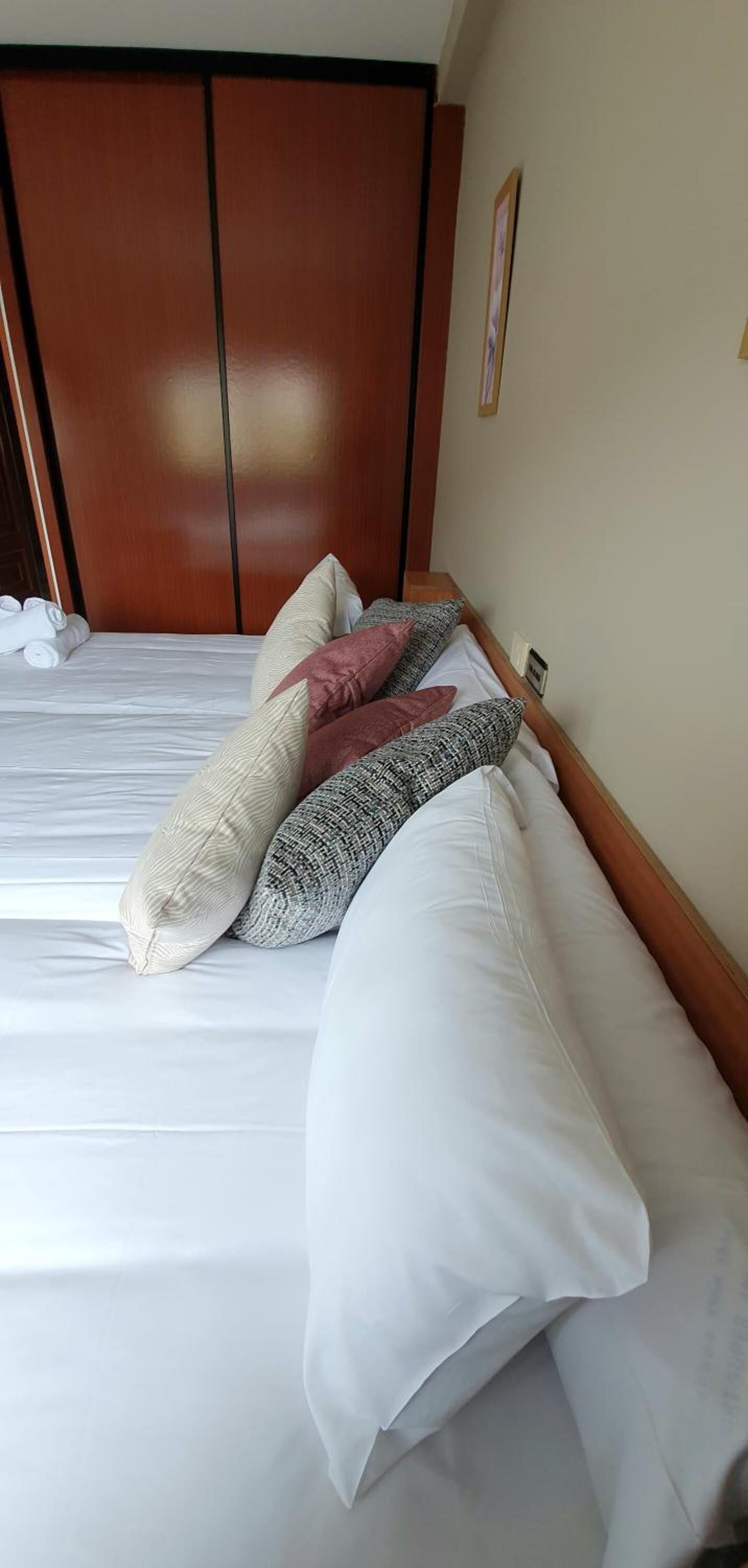 A neatly made bed with white and patterned pillows, a wooden headboard, and a framed picture on the wall.