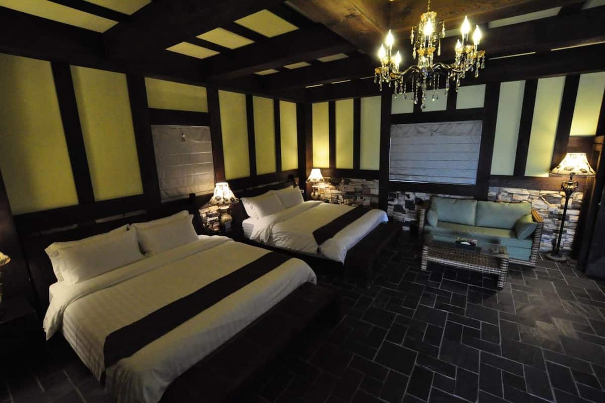 A hotel room with two beds, a chandelier, a sofa, and a tiled floor.