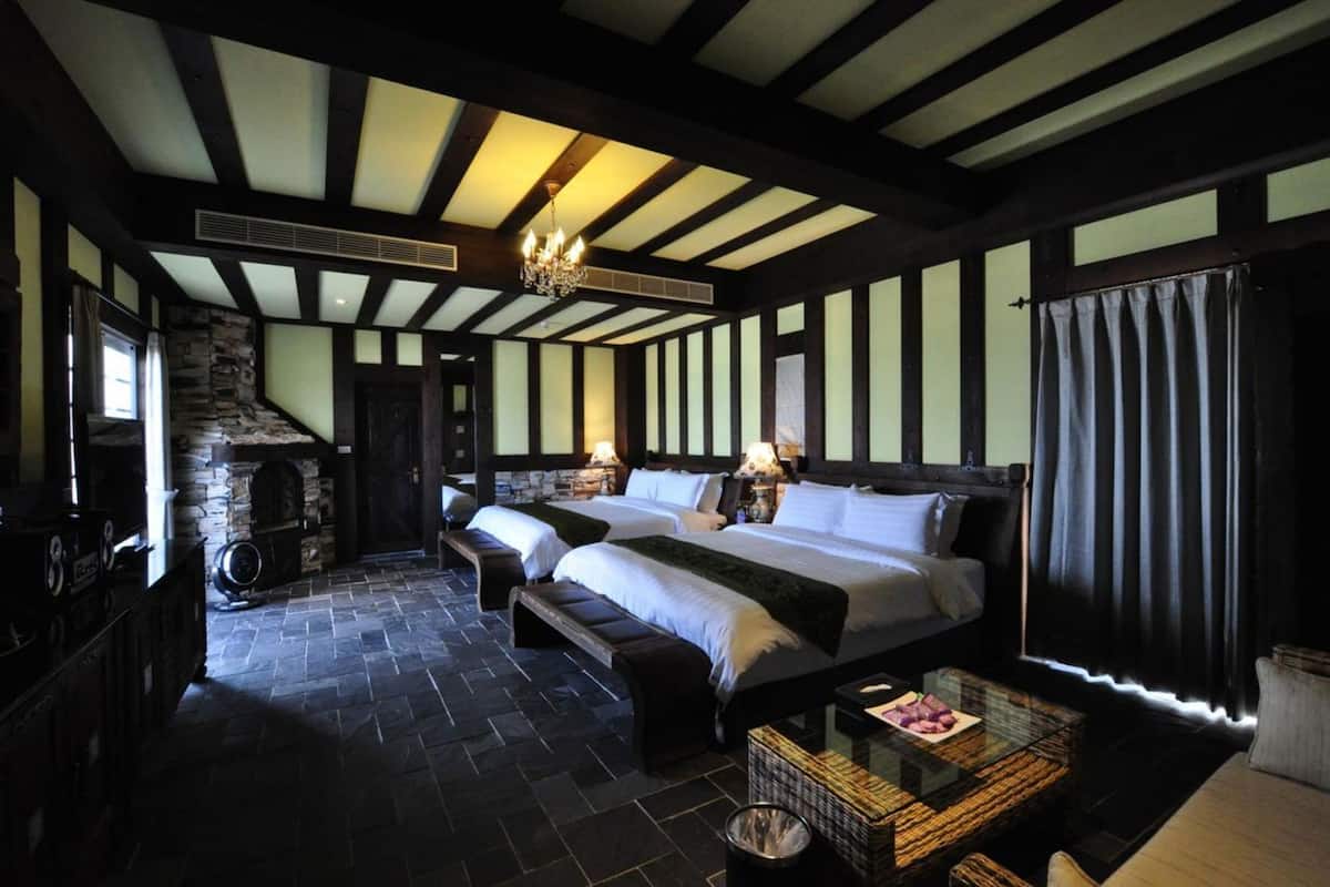 A room with two beds, a stone fireplace, and a wooden ceiling.