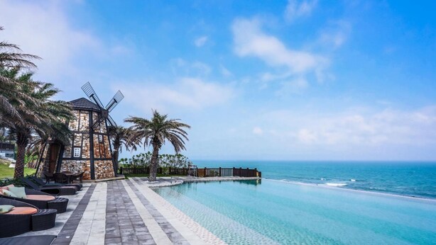 A beachfront hotel with a windmill, infinity pool, and palm trees. - Stuart Villa (Shoufeng)