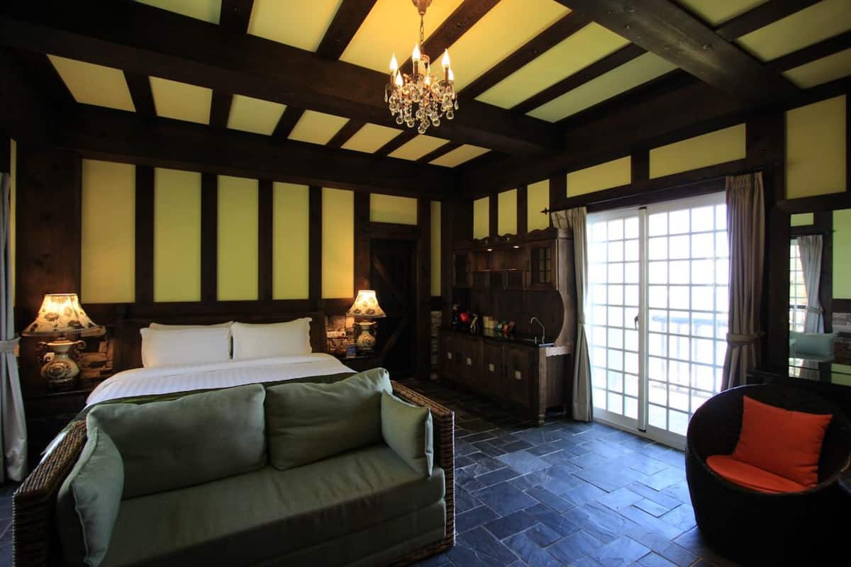 A traditional room with a bed, a green sofa, a wicker chair, a wooden cabinet, and a chandelier.