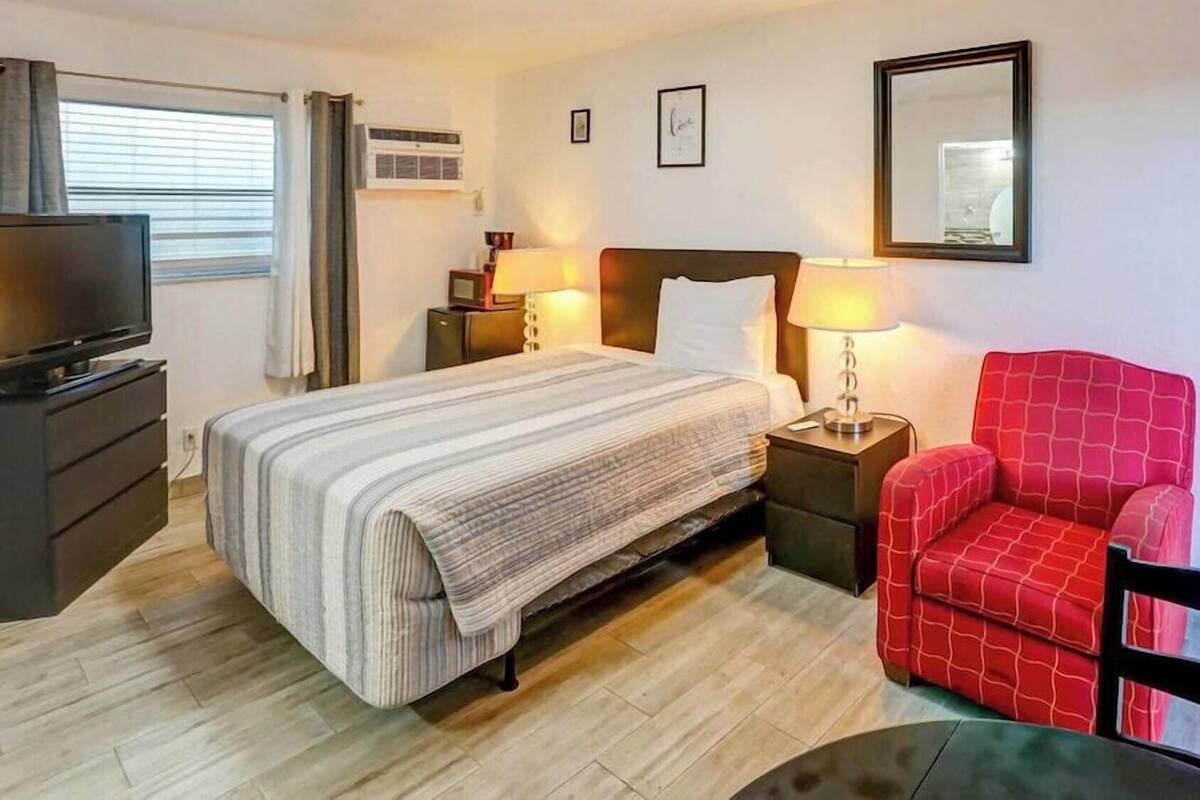A hotel room with a bed, a TV, a chair, a table, and a mirror.