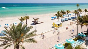 A beach with clear turquoise water, palm trees, and beach umbrellas. - Richards Motel Courtyard (Hollywood)