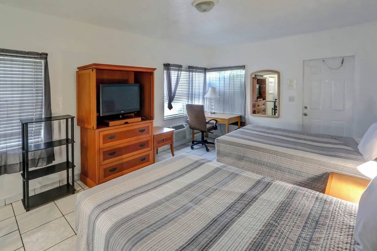 A hotel room with two beds, a TV on a wooden cabinet, a desk with a chair, and a mirror on the wall.
