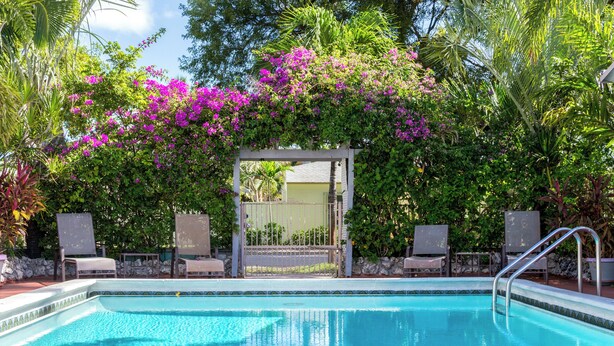 A swimming pool with a pergola covered in purple flowers, surrounded by chairs and lush greenery. - Richards Motel Courtyard (Hollywood)