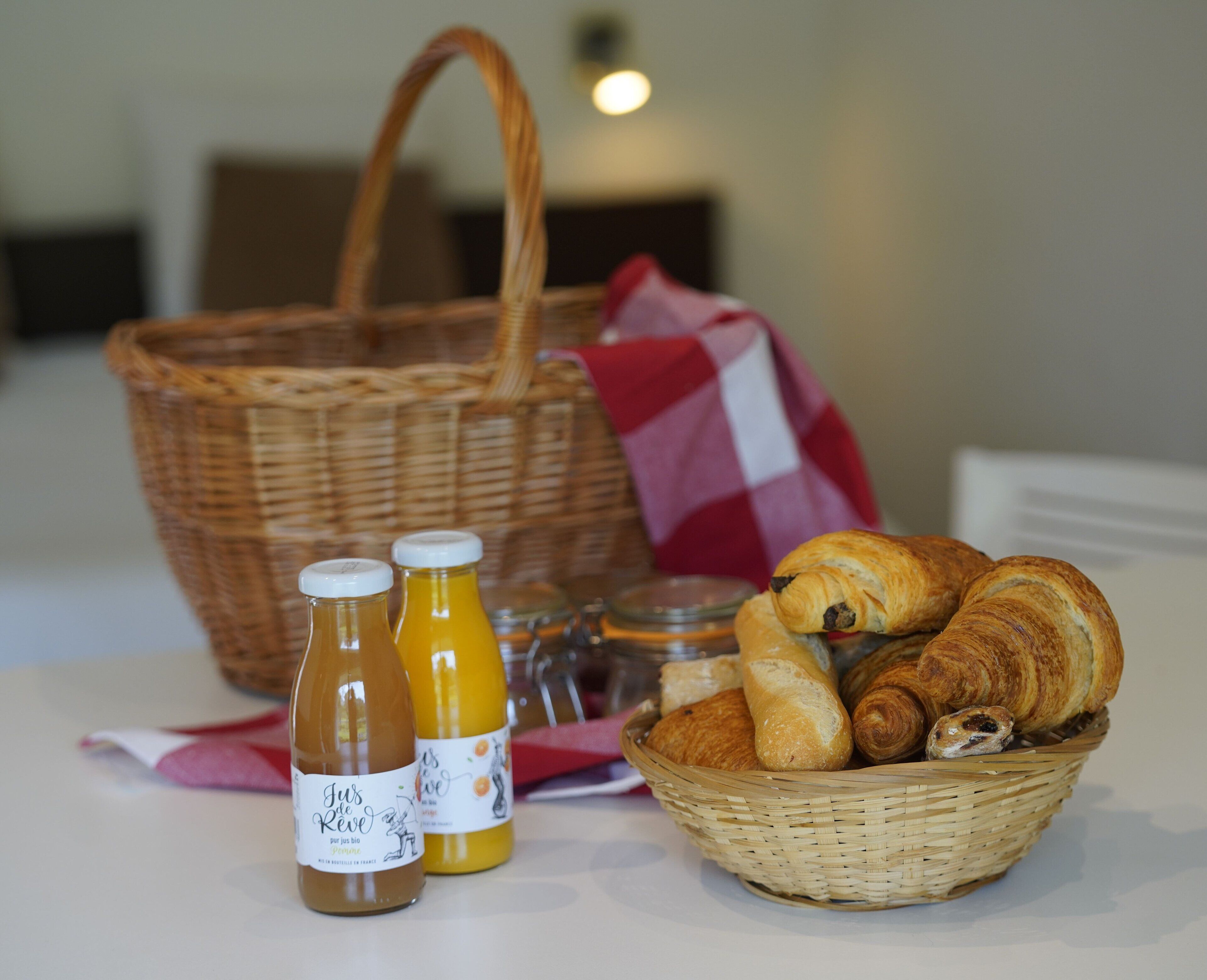Una cesta de mimbre llena de croissants y una botella de jugo sobre una mesa.