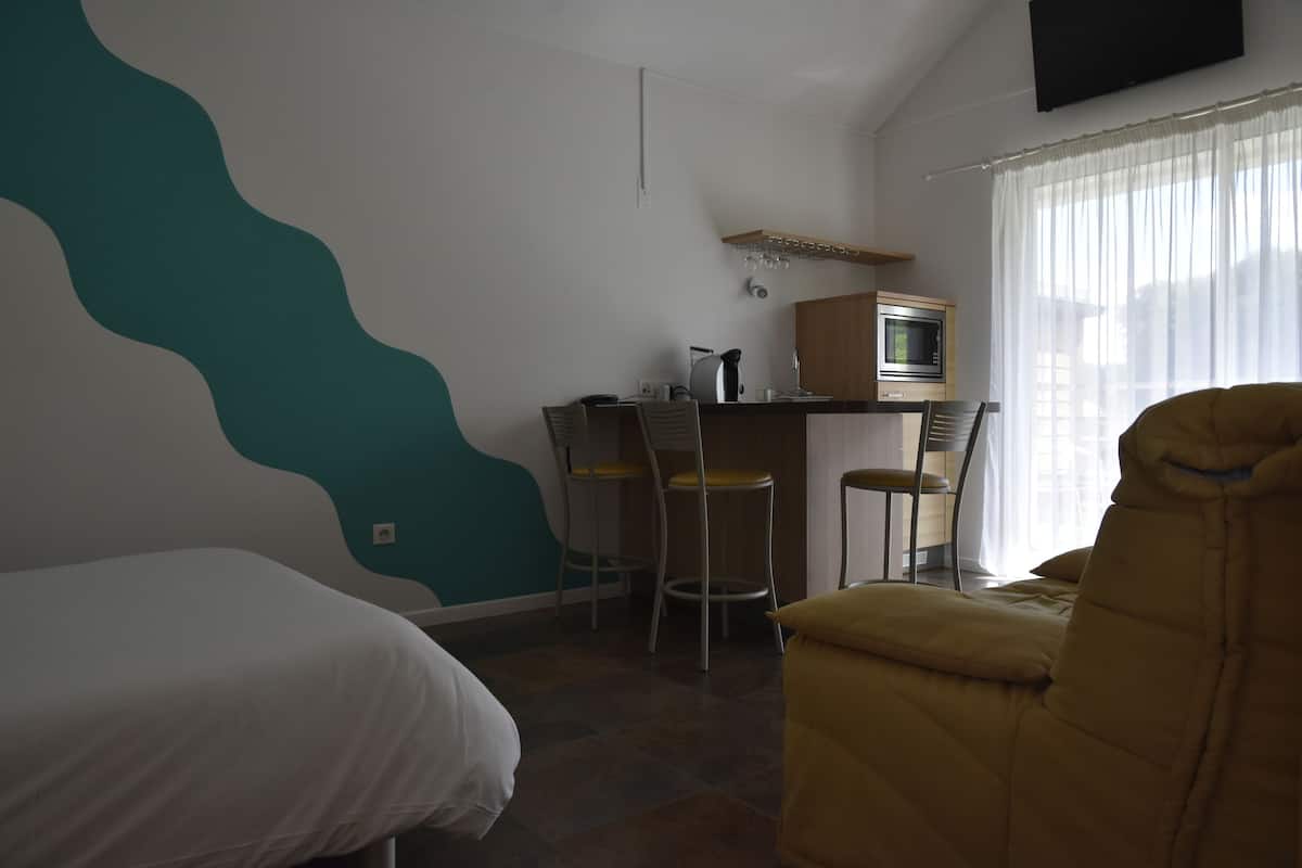 Una habitación con cama, un escritorio con computadora, una silla y un televisor en la pared.