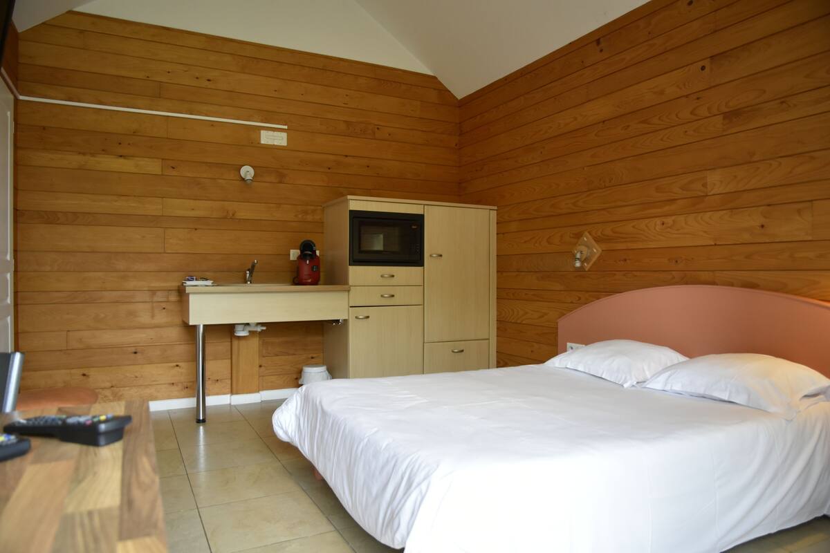 Un dormitorio con techo de madera, una cama con ropa de cama blanca, un armario de madera y una pequeña zona de kitchenette.