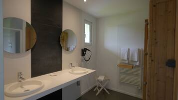 A modern bathroom with two sinks, large mirrors, a towel rack, and a wooden door.