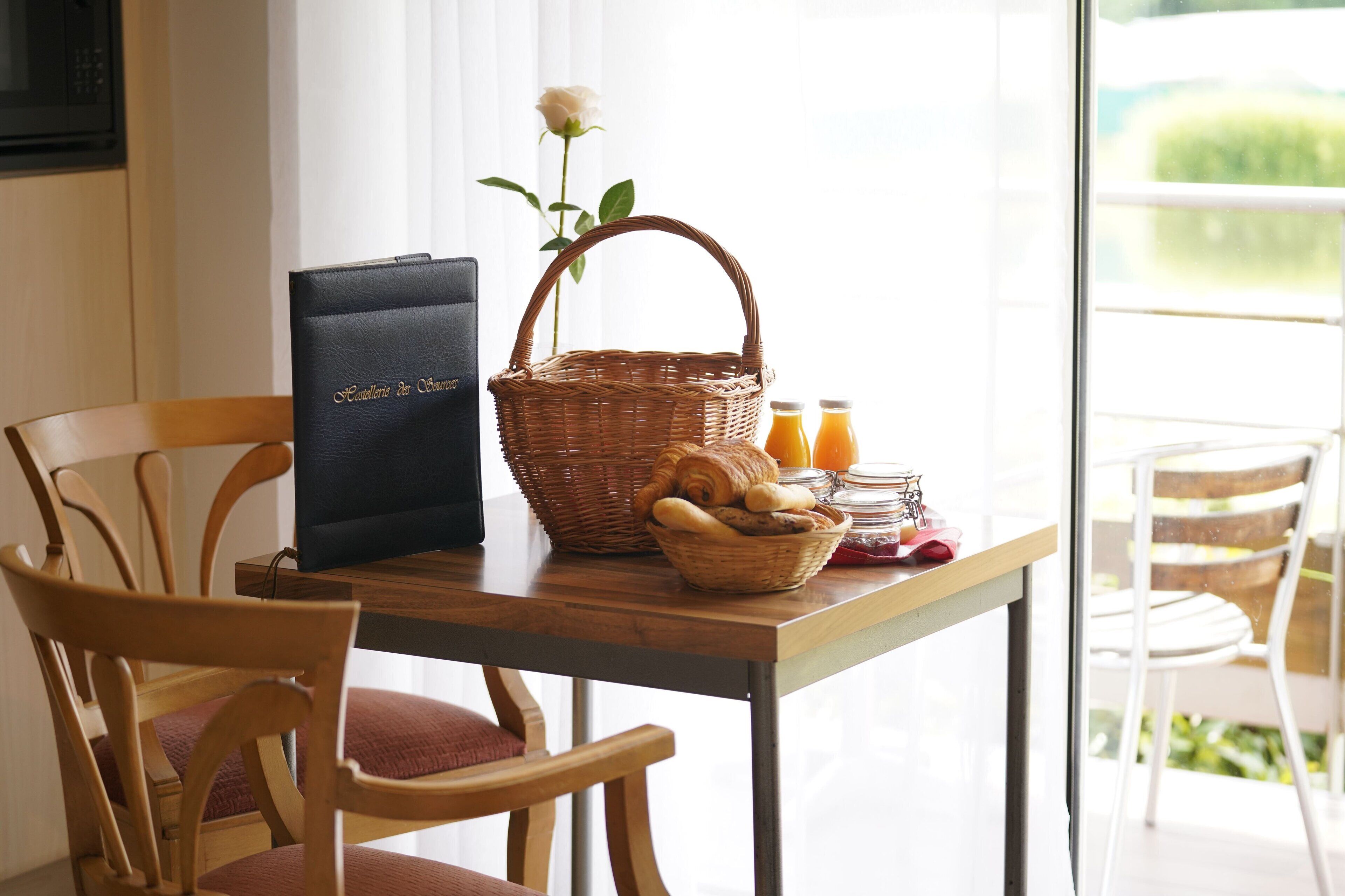 A wooden table with a wicker basket, a bouquet of flowers, and a glass of orange juice.