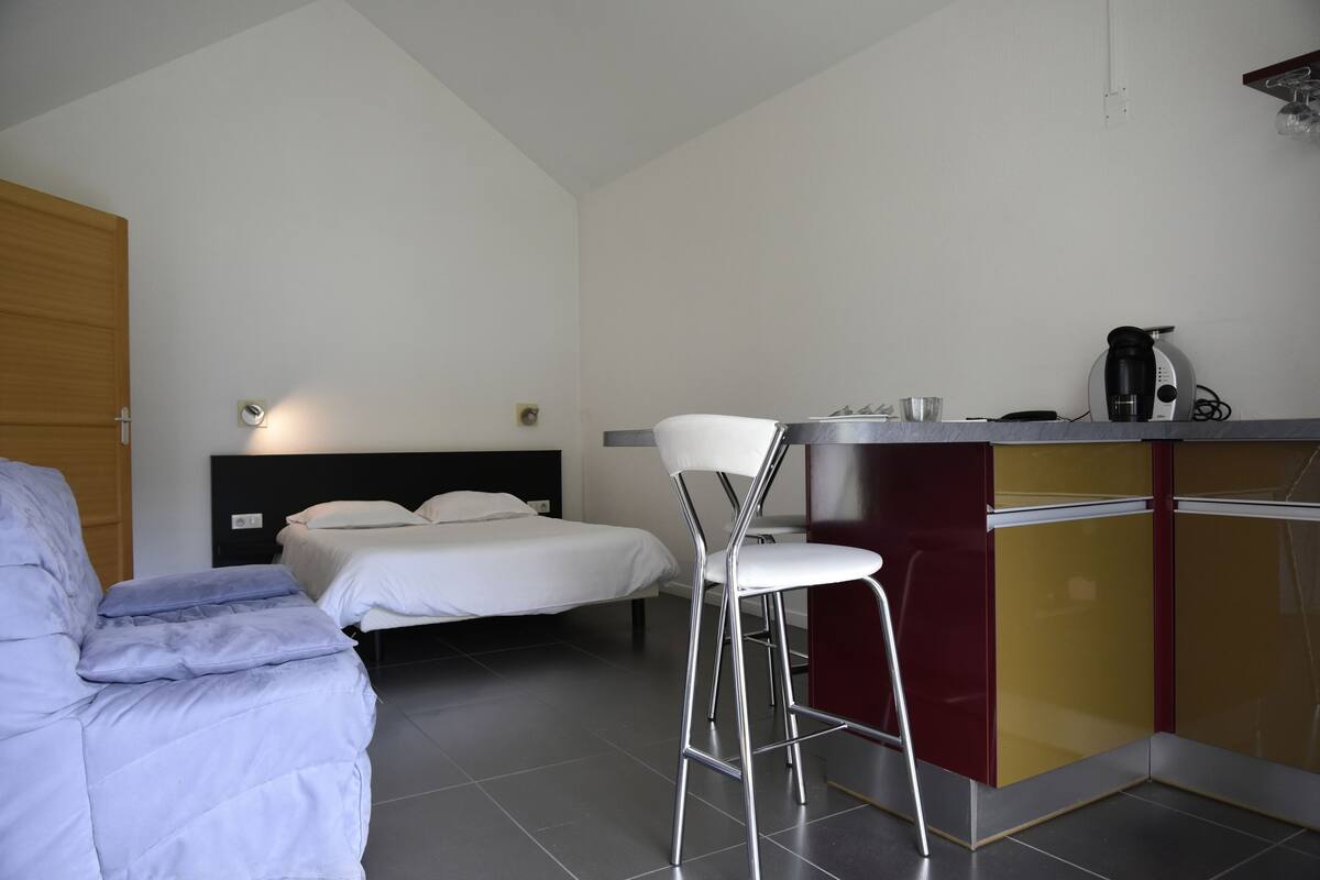 Un dormitorio con una cama, una silla, un escritorio con cafetera y un armario.