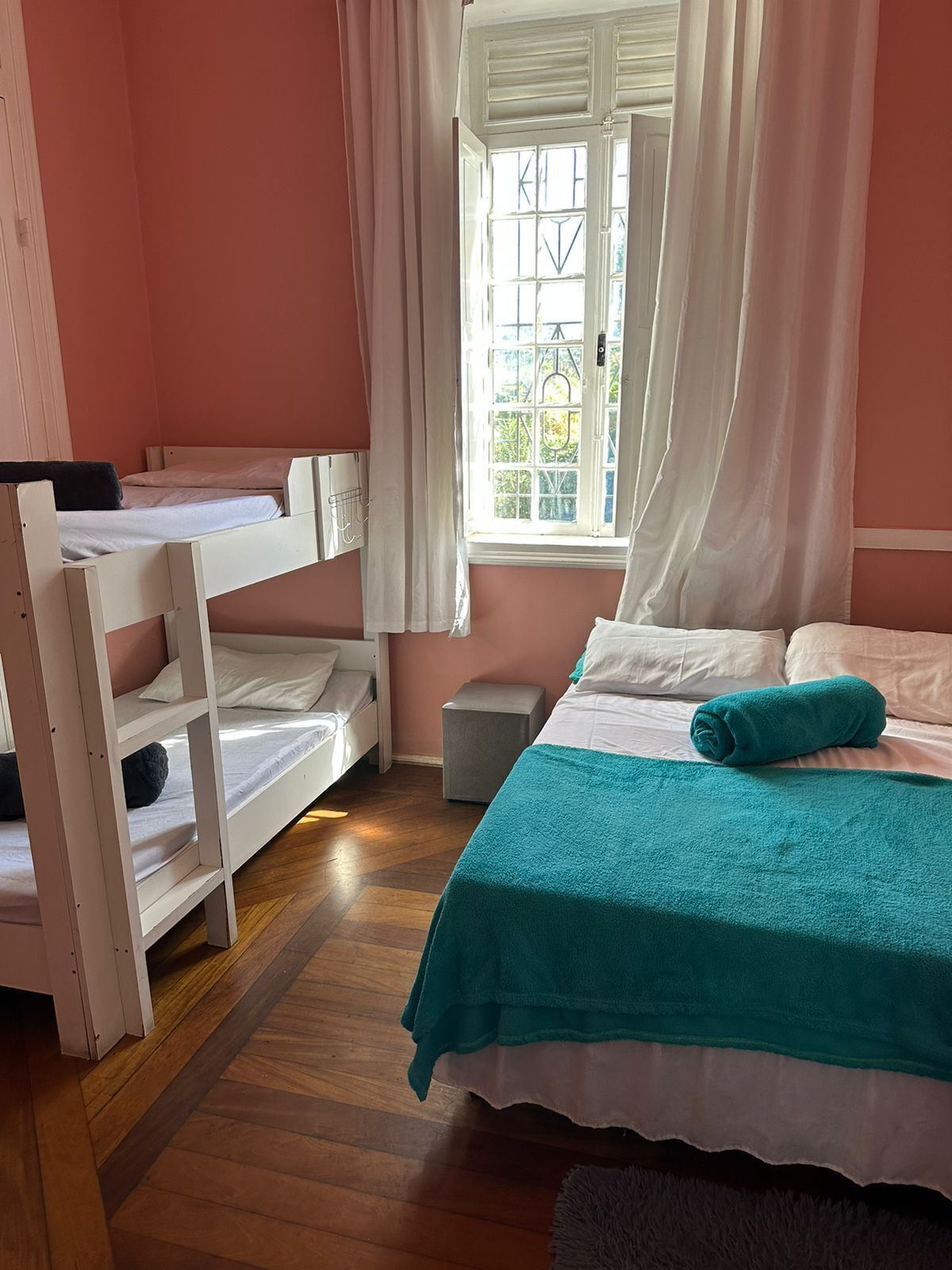 Un dormitorio con una cama litera, una cama individual, una ventana con cortinas y vistas a zonas verdes.