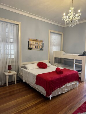 A bedroom with a bed, a small table, a chandelier, and a bunk bed. - Hotel Cidade Imperial (Petrópolis)