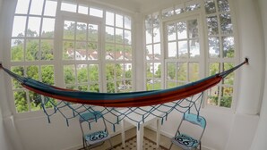 A hammock suspended between two windows in a room with a view of greenery and houses. - Hotel Cidade Imperial (Petrópolis)