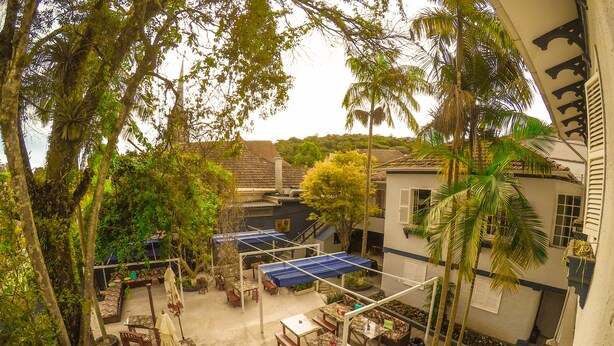An outdoor patio area with tables and chairs, surrounded by trees and buildings. - Hotel Cidade Imperial (Petrópolis)
