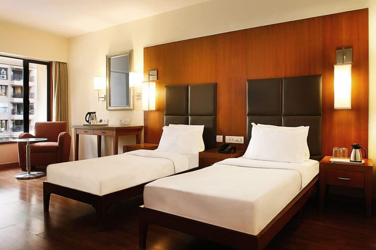 Une chambre d’hôtel avec deux lits simples, un bureau, une chaise, une machine à café et une vue sur un bâtiment à l’extérieur.