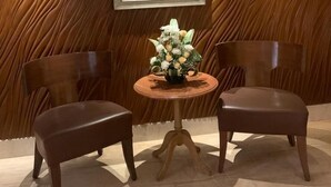 A room with a wooden textured wall, a round table with a floral centerpiece, and two dark brown chairs. - The Classique Club (Mumbai)