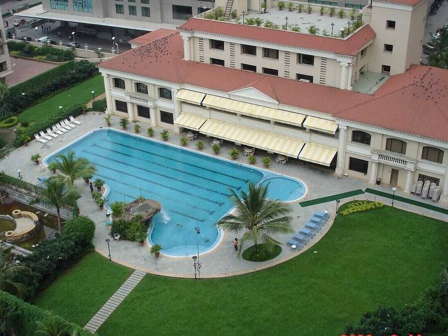 Et hotel med en stor swimmingpool, en velholdt græsplæne og et overdækket udendørs opholdsområde.
