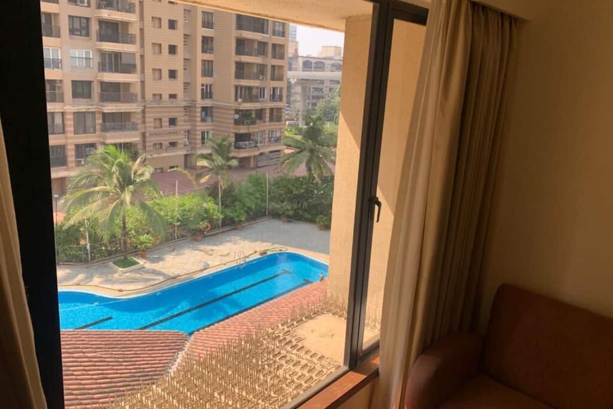 Une pièce dotée d’une grande fenêtre donnant sur une piscine et offrant une vue sur un quartier résidentiel composé de plusieurs immeubles.