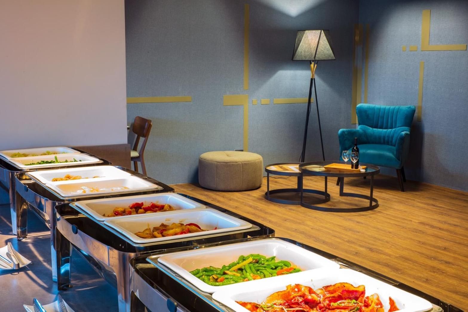 A buffet setup with various food items, a lamp, a blue chair, and a round table.