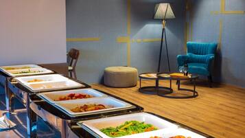 A buffet setup with various food items, a lamp, a blue chair, and a round table.