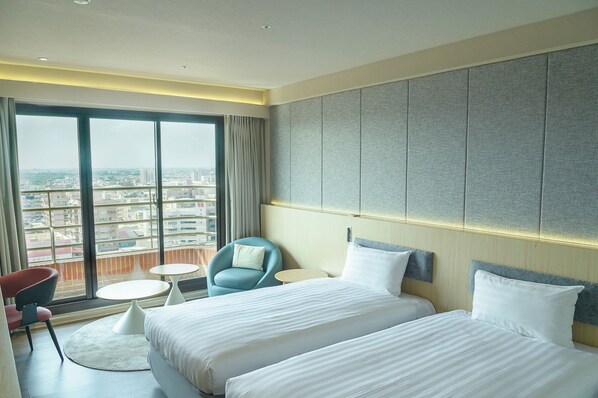 A hotel room with a large window, two beds, a chair, a small table, and a view of the city.
