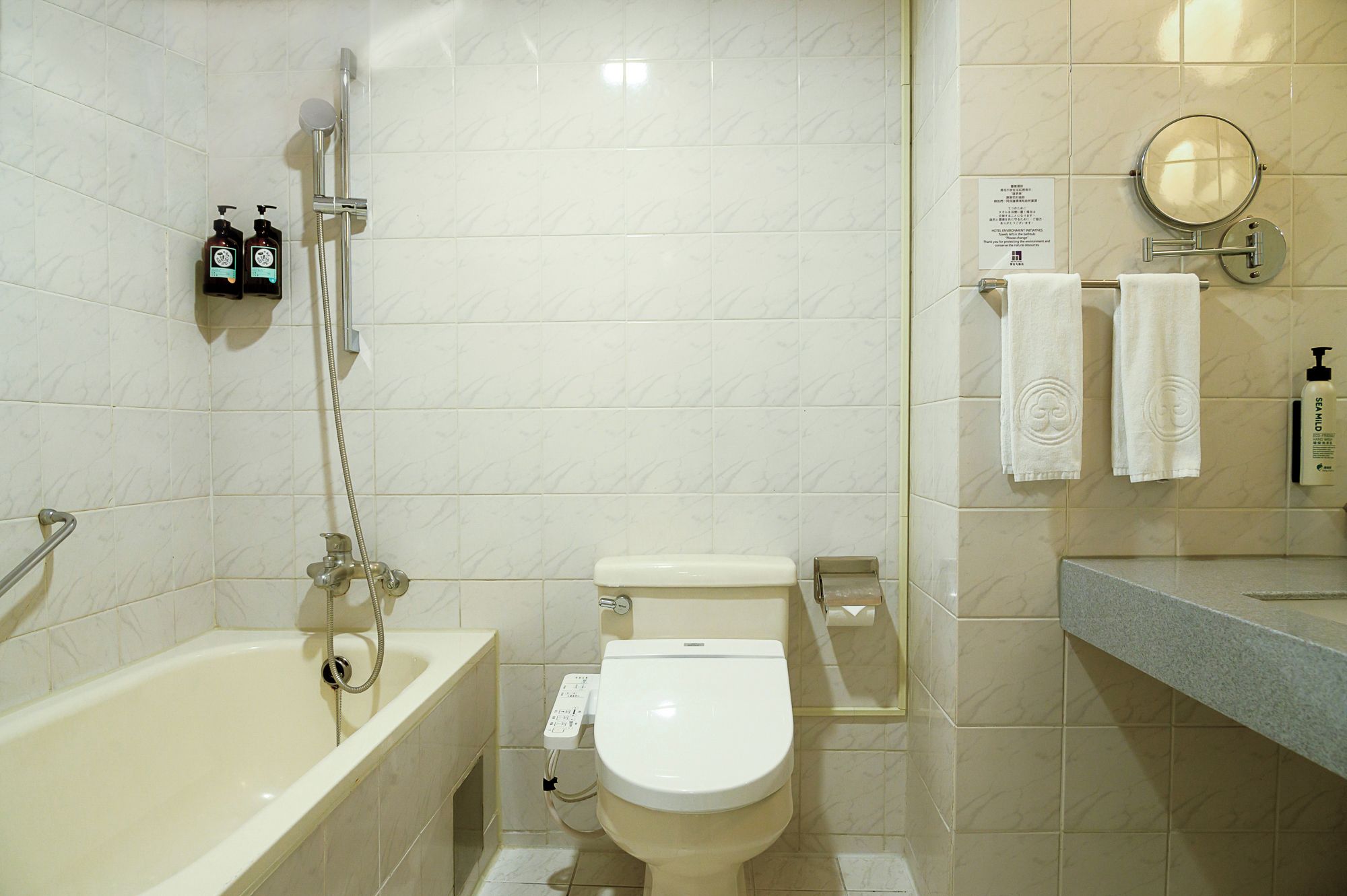 Un baño con bañera, inodoro y ducha. Hay dos botellas de champú en la pared.